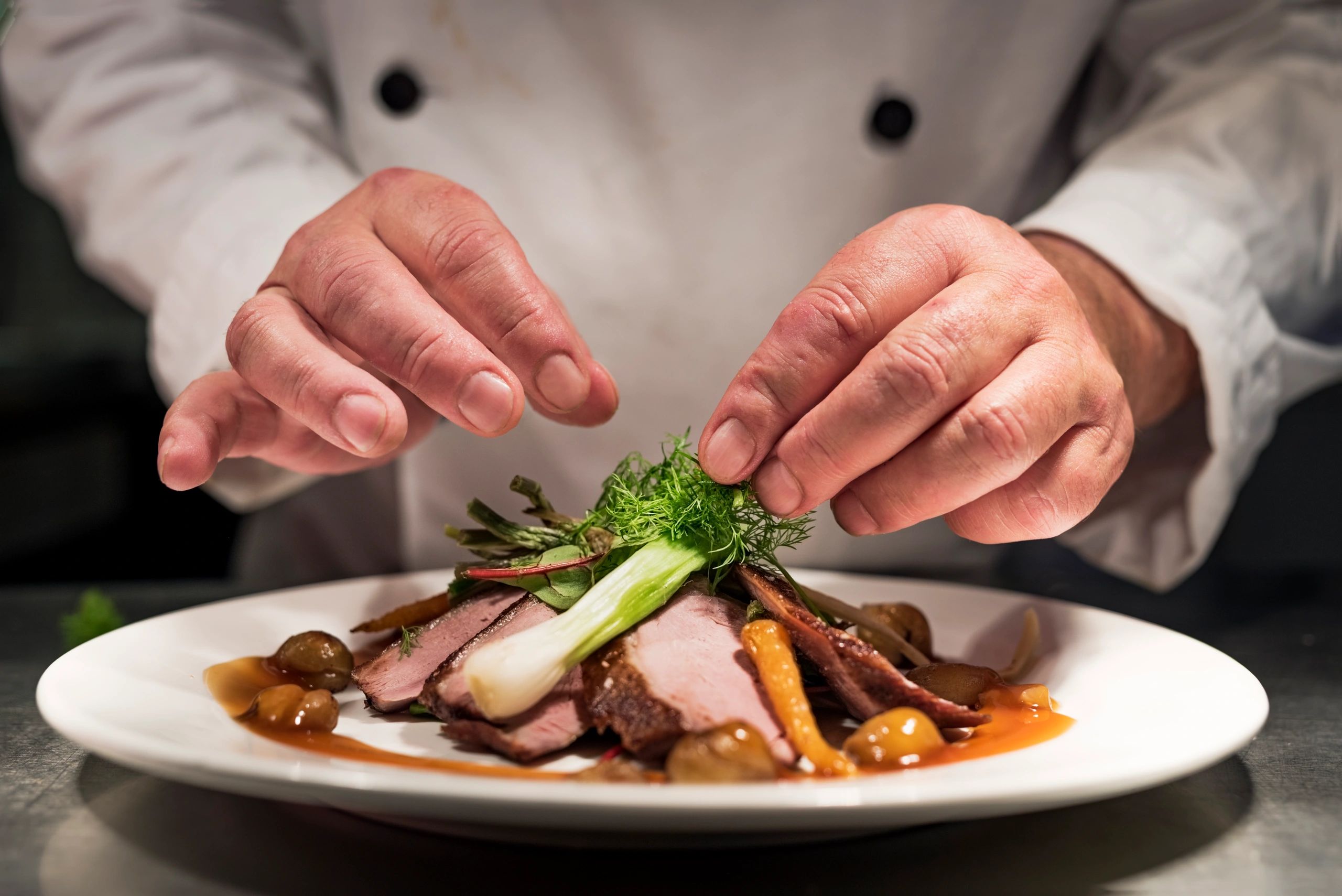 Chef hands plating a dish at the pass